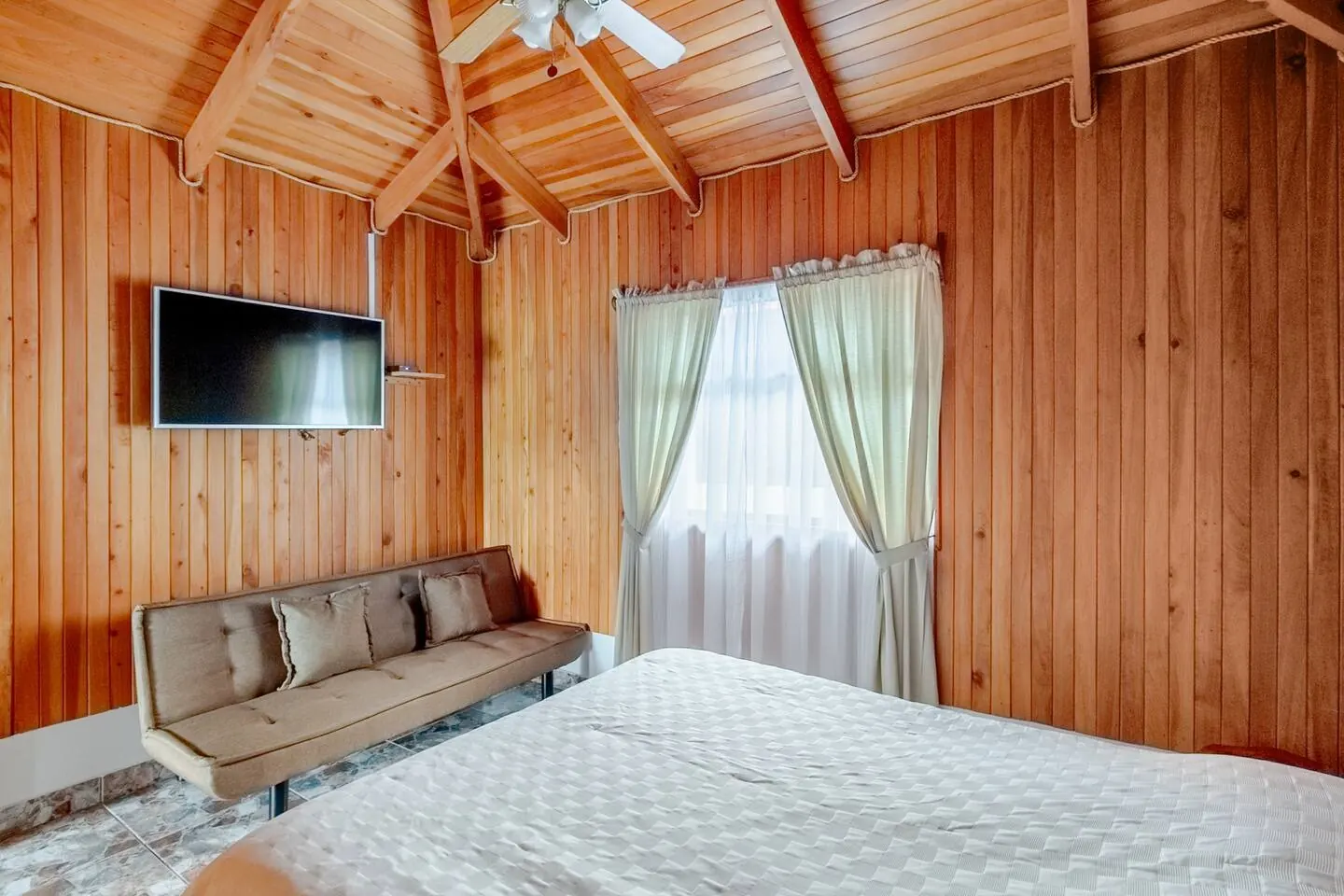 Poas Cottage bedroom with wood-paneled walls, bed, and lounge futon